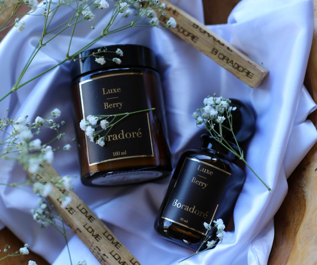 Boradoré Luxe Berry scented candle and reed diffuser styled on white fabric with delicate flowers
