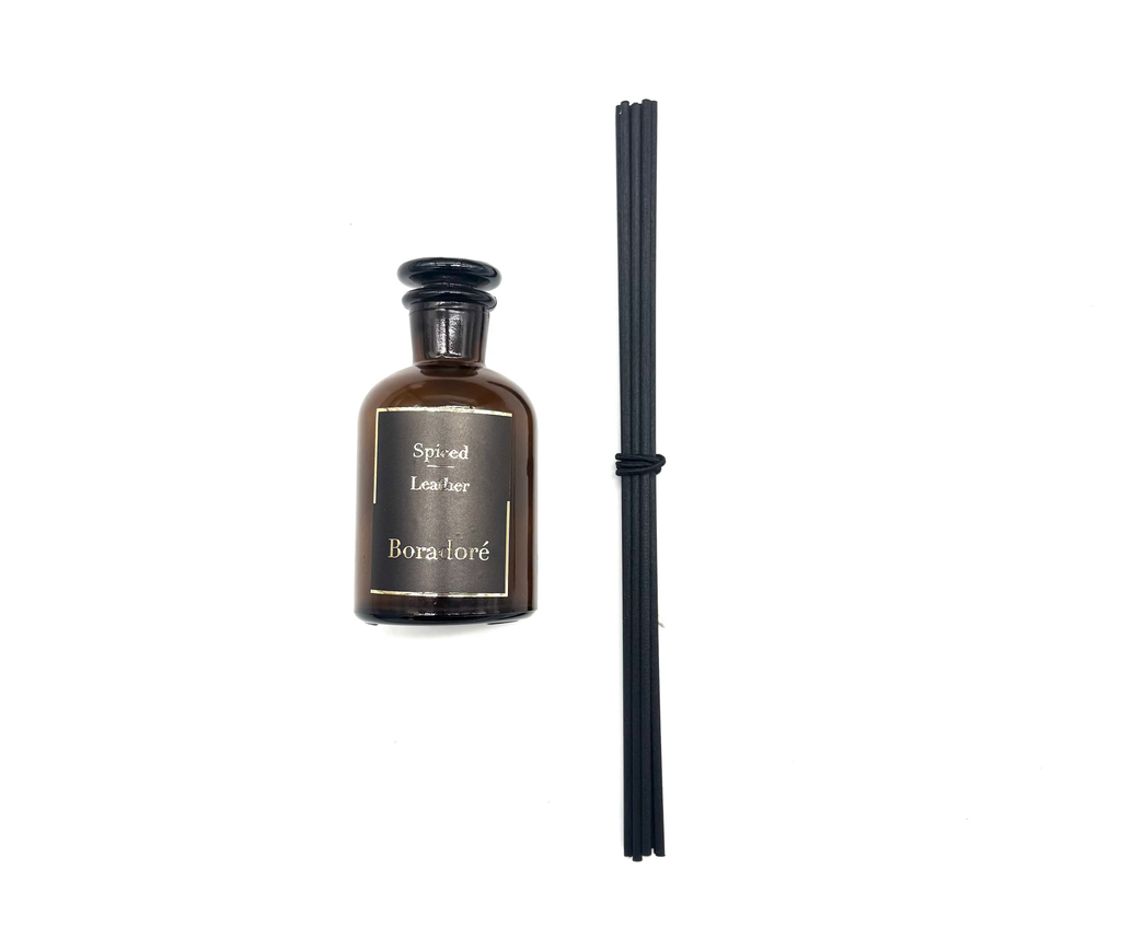 Boradoré Spiced Leather reed diffuser bottle with black sticks on a white background
